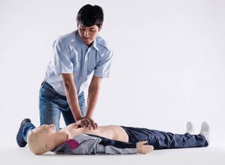 A healthcare trainer performing CPR training on an adult medical simulation manikin for a community advocacy program.