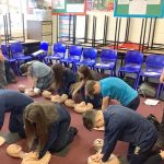Students in an Irish classroom practicing lifesaving bystander CPR on mannequins as part of a school training program.
