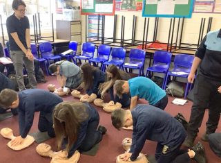 Students in an Irish classroom practicing lifesaving bystander CPR on mannequins as part of a school training program.