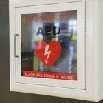 A person opens an AED storage cabinet.
