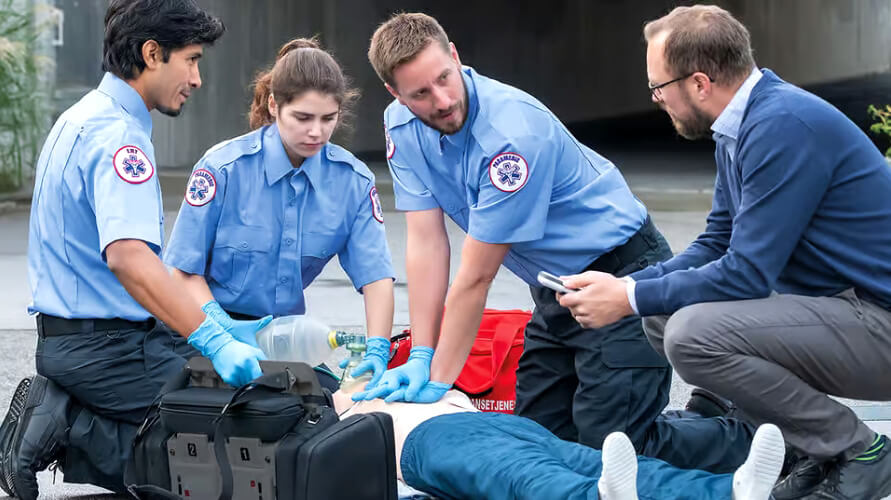 Three EMTs perform CPR and emergency resuscitation on a patient on the ground while a bystander assists