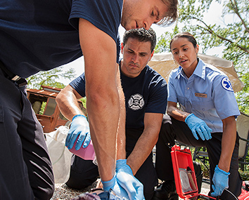 Prehospital emergency responders providing medical assistance to a patient lying on the ground during an outdoor emergency scenario.