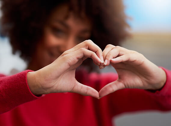 Person in a red sweater forms a heart shape with their hands.