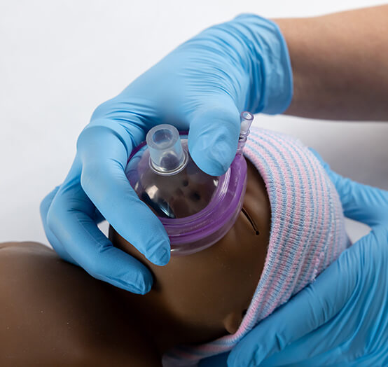 Gloved hands administering oxygen mask to newborn during neonatal resuscitation