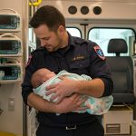 Paramedic holding newborn infant inside ambulance after out-of-hospital delivery