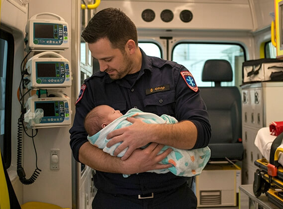 Paramedic holding newborn infant inside ambulance after out-of-hospital delivery