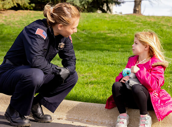 EMS provider kneeling at eye level to calmly reassure a young girl during a pediatric emergency call.